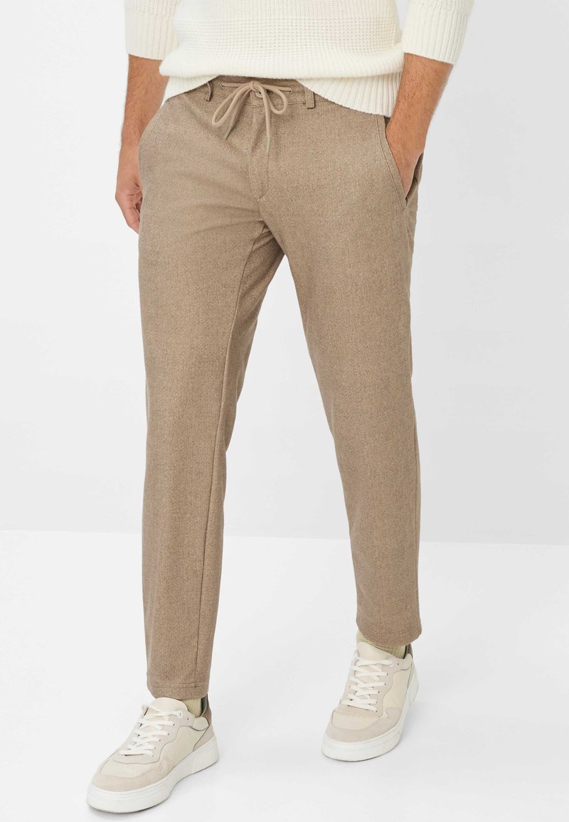 Lichtbruine broek met een gestructureerde afwerking, een tailleband met elastiek en koord, en zijzakken, gecombineerd met witte en beige sneakers.