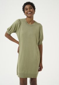 Abito a maglia a maniche corte di colore verde chiaro. Presenta un collo rotondo a coste e orlo. La silhouette è rilassata e leggermente oversize.