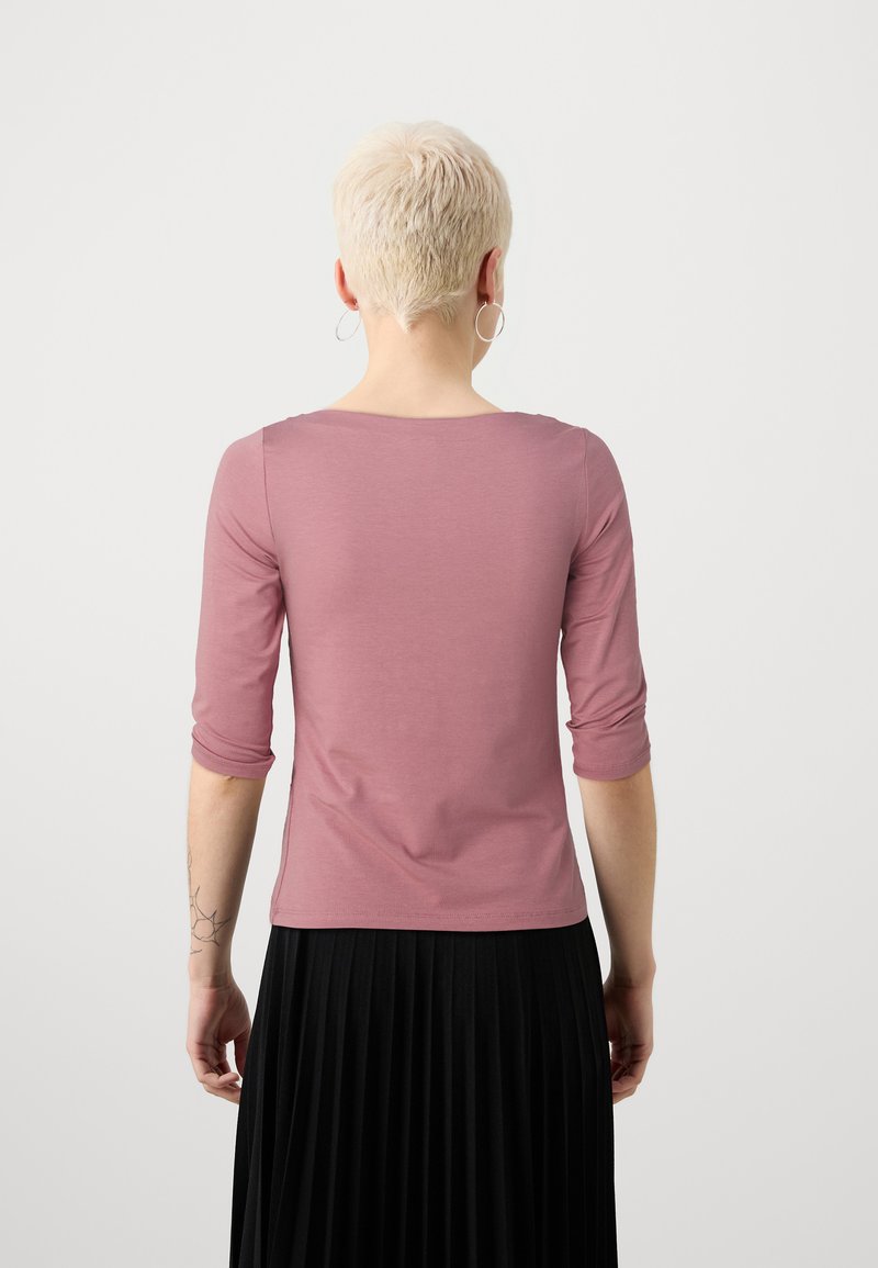 Langärmliges Oberteil aus weichem pinken Stoff, mit rundem Halsausschnitt und tailliertem Schnitt, kombiniert mit einem plissierten schwarzen Rock.