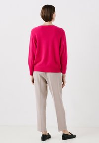 Maglione fucsia a maglia con maniche lunghe, vestibilità rilassata e polsini a costine, abbinato a pantaloni beige chiaro e scarpe nere.