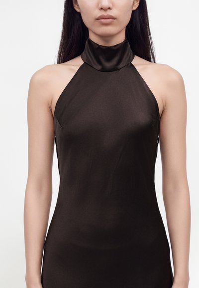 Femme portant une robe en satin noire sans manches à col licou, montrée des épaules aux hanches sur un fond clair uni.