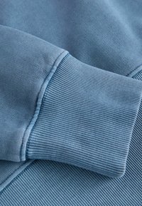 Tessuto di felpa azzurro chiaro con polsini a costine e una superficie liscia, caratterizzato da dettagli di cucitura lungo i bordi.