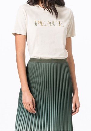 Chemise crème à manches courtes avec le mot "PAIX" en fleurs, associée à une jupe plissée verte. La jupe présente une texture lisse et une taille élastique.