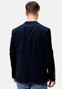 Marineblå kordfløyelsblazer med teksturert overflate, enkelt vent bak og knappdetaljer på ermene. Skreddersydd passform med skarpe revers.