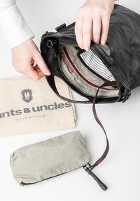 Zwarte leren tas met een gestreepte voering, een tankleurige stoffen zak en een grijze gestreepte ritscase, die verschillende texturen en materialen toont.