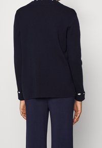 Marinblå stickad tröja med en avslappnad passform, rundad halsringning och knäppte ärmslut. Mjuk textur med subtila detaljer på ärmsluten.