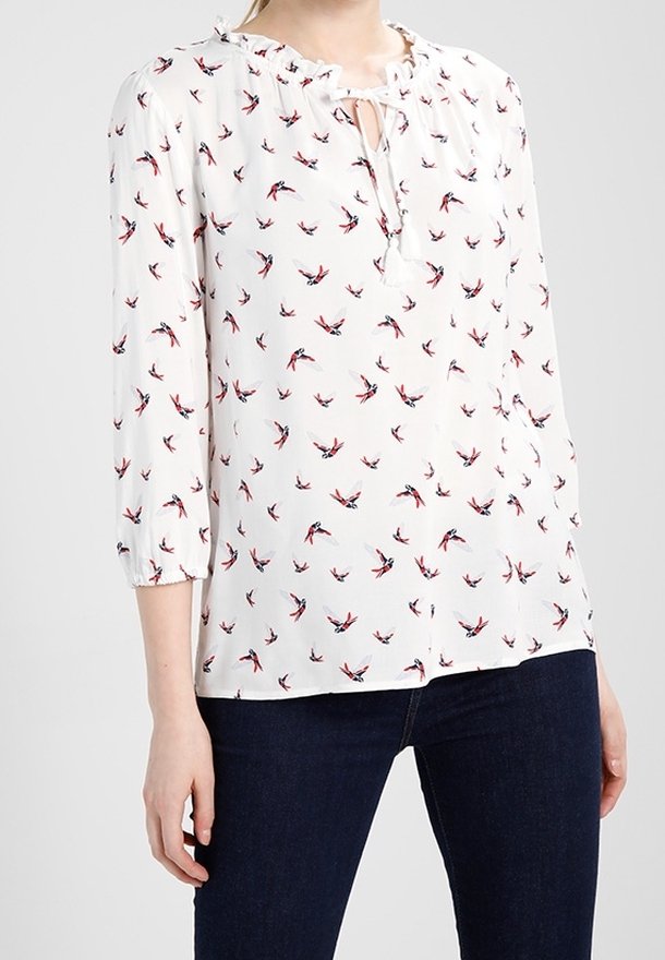 White blouse with red and blue bird pattern, gathered neckline, and three-quarter sleeves. Lightweight fabric with a relaxed fit.