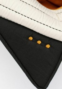 Črna tkanina z bež zgornjo robno linijo. Poudarjeno s kontrastnim črnim šivom in tremi majhnimi zlatimi pikami blizu dna.