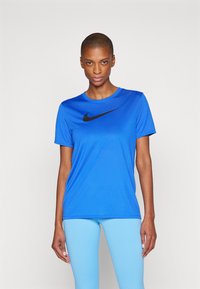 Sininen urheilupaita lyhyillä hihoilla, jossa on musta Nike-logon swoosh etupuolella. Tasainen, kosteutta siirtävä kangas.