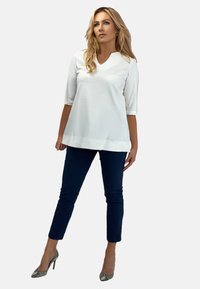 Biała bluzka z trzema czwarte rękawami, z dekoltem w kształcie litery V i lekko skróconym dołem; połączona z granatowymi spodniami slim fit i wzorzystymi szpilkami.