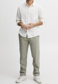 Chemise boutonnée beige clair à manches longues, associée à un pantalon vert clair et des baskets blanches ; tissu décontracté avec une coupe relax.}}