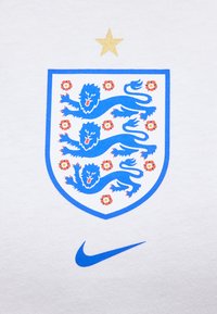 Τρία μπλε λιοντάρια και έμβλημα ασπίδας με κόκκινες τριανταφυλλιές, ένα χρυσό αστέρι από πάνω και ένα μπλε λογότυπο Nike σε λευκό ύφασμα.