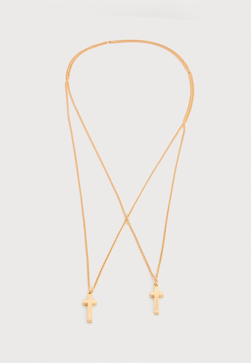Collier en ton or avec deux petits pendentifs en forme de croix, reliés par des chaînes délicates sur un fond blanc uni.