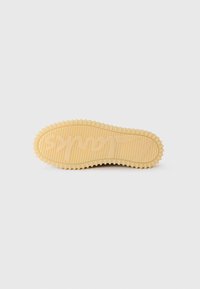 Gummisåle i lys beige med rillet tekstur. Har et merket logo og bølgede kanter for grep.