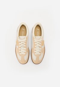 Bežīgi un krēmkrāsas sneakers ar strukturētu augšdaļu, auklu aizdari un gumijas zoli. Satur logotipu un izteiktu šuvju akcentus.