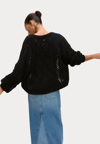 Svart stickad tröja med en lös, oversized passform, prydd med ett diamantt mönster och ribbad nederkant, kombinerad med en ljusblå denimkjol.