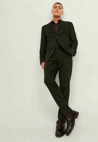 Tummanvihreä räätälöity puku, jossa on viistot kaulukset, yhdistettynä tummanpunaiseen paitaan. Omistaa slim fit -leikkauksen ja sileän pinnan; täydentää ruskeat loafers-kengät.