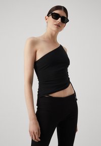 Top nero a spalla unica realizzato in materiale aderente con texture arricciata, abbinato a leggings neri a vita alta. Design semplice ed elegante.