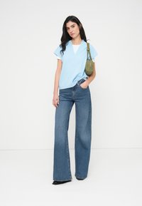 Ανοιχτό μπλε κορυφή με κοντά μανίκια και V-λαιμόκοψη, συνδυασμένη με φαρδιά μπλε τζιν παντελόνια. Αξεσουάρ περιλαμβάνει μια μικρή πράσινη τσάντα χιαστί.