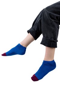 Niebieskie skarpetki za kostkę z bordowymi końcówkami, ściśle dopasowane, wykonane z miękkiego materiału, noszone z czarnymi podwiniętymi dżinsami, pokazującymi gładką fakturę powierzchni.