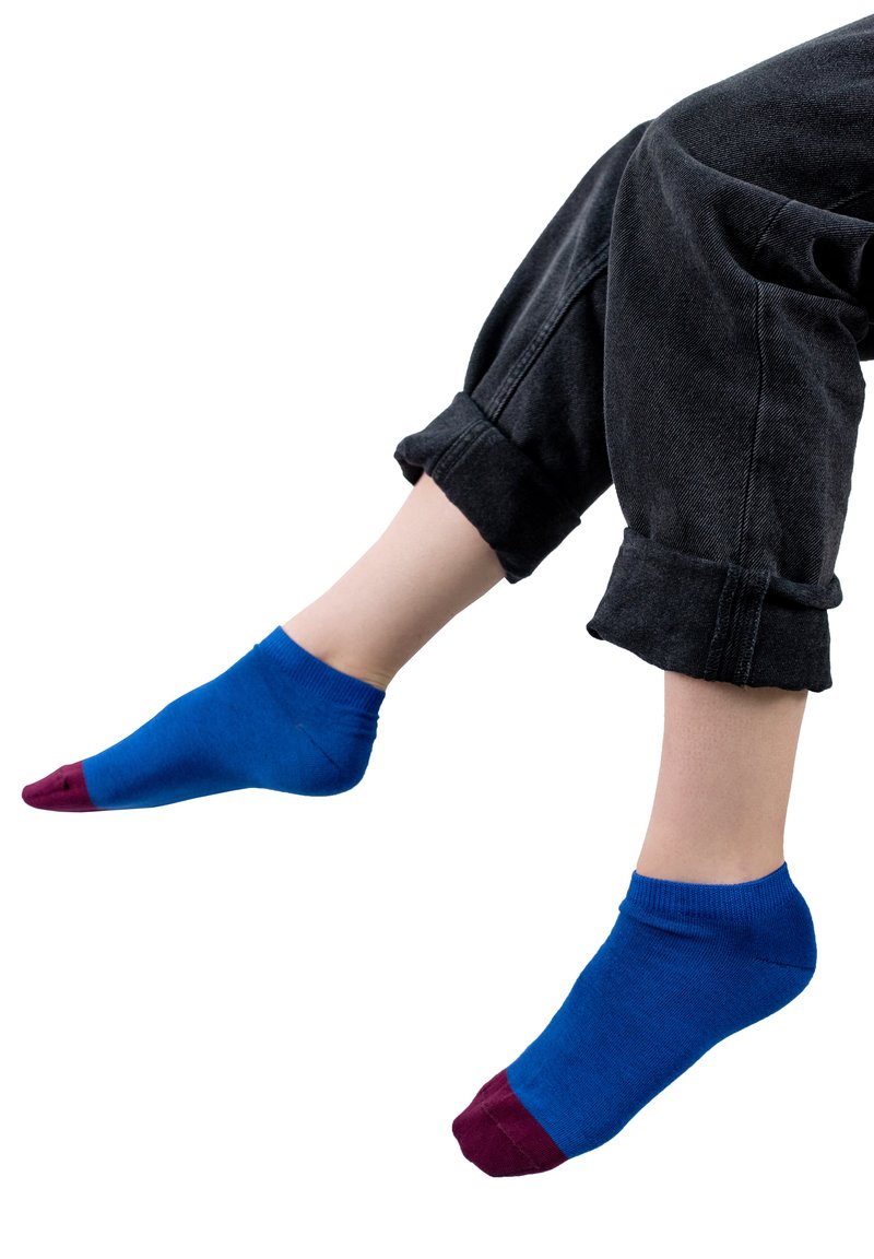 Niebieskie skarpetki za kostkę z bordowymi końcówkami, ściśle dopasowane, wykonane z miękkiego materiału, noszone z czarnymi podwiniętymi dżinsami, pokazującymi gładką fakturę powierzchni.