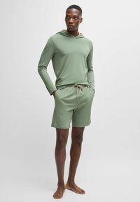 Lichtgewicht olijfgroen langarmshirt met capuchon, gecombineerd met bijpassende short met trekkoord. Zachte textuur, casual pasvorm en minimale logo details.