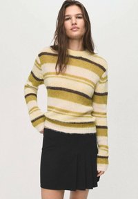 Maglione a righe giallo, verde e marrone con un design aderente e maniche lunghe, abbinato a una gonna nera plissettata. Texture morbida.