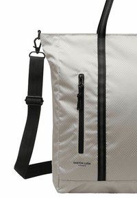 Borsa tote grigia chiara realizzata in tessuto testurizzato, caratterizzata da una tasca con zip nera, una tracolla regolabile e strisce nere a contrasto.