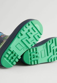 Baskets pour enfants avec une tige bleu marine, un design à motifs et une semelle en caoutchouc verte présentant un motif texturé pour une bonne adhérence et traction.