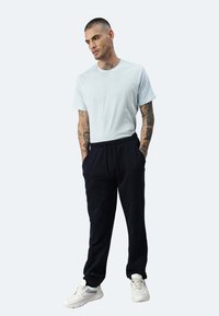 Hellblaues T-Shirt, schwarze Jogginghose mit elastischem Bund und weiße Sneaker. Das Outfit ist lässig mit einer lockeren Passform und kurzen Ärmeln.