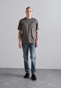 Gray striped short-sleeve t-shirt with a relaxed fit, paired with light blue denim jeans and black sneakers, against a neutral background.
