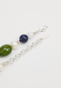 Perlenarmband mit grünen, weißen und blauen Steinen, silbernem Zubehör und einer verlinkten Kette mit einem Karabinerverschluss und einem Markenschild.