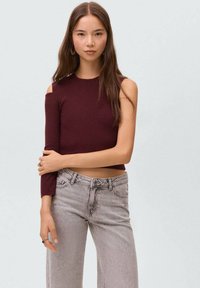 Bordeaux pleteni crop top z eno dolgo rokav in enim izrezom na rami; kombiniran z svetlo sivo širokima hlačami. Minimalistična zasnova, mehak material.