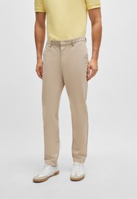 Beige trousers made of lightweight fabric, featuring a straight leg design, standard waistband, and front pockets, paired with white sneakers.