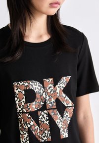 Černé bavlněné tričko s velkým nápisem "DKNY" v leopardoím vzoru v hnědé a krémové barvě. Krátké rukávy, design s kulatým výstřihem.