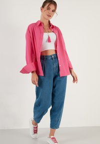 Pink long-sleeve shirt, buttoned, paired with high-waisted blue denim jeans. White sneakers with red laces. Textured fabric and relaxed fit.