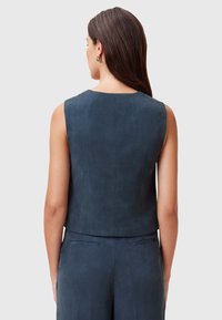 Marinblå ärmlös topp med en slät, mockaliknande textur, som har en rundad halsringning och en kort design som visar detaljer på ryggen.
