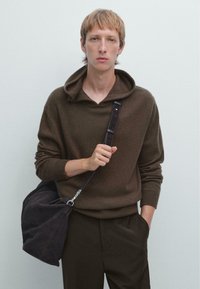 Bruine gebreide hoodie met een ruime halslijn en lange mouwen. Gecombineerd met donkere broeken en een zachte, donkere schoudertas. Soepele textuur.