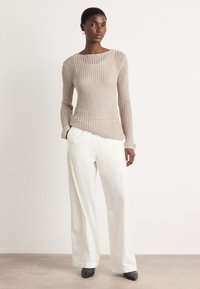 Beige knitted sweater with a wide neckline, paired with loose white trousers, featuring a smooth texture and a relaxed fit. Black heels complete the outfit.