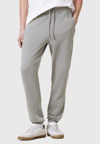 Grå sweatpants med en mjuk textur, elastisk midja, snörning och sidofickor. Matchas med vita sneakers med en beige sula.