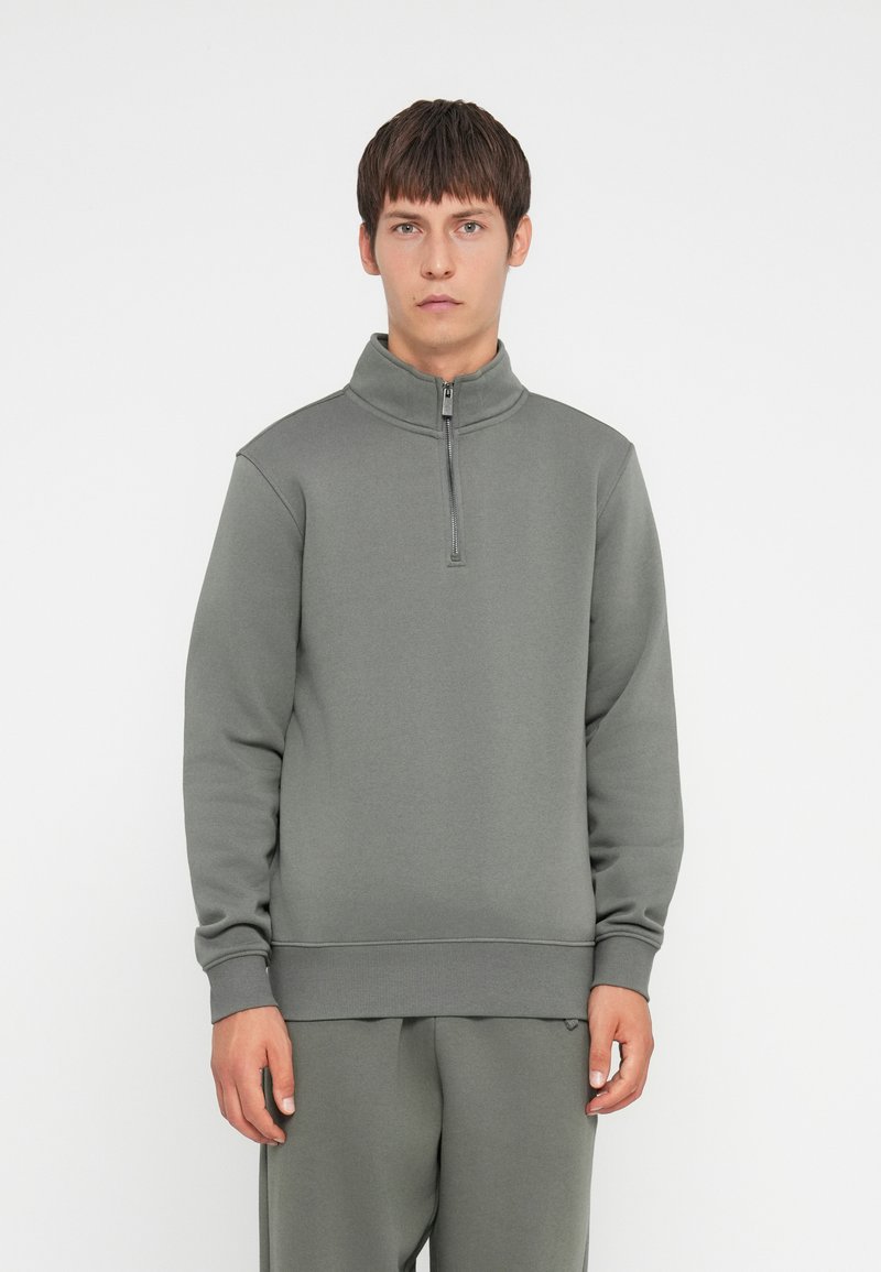 Grijze sweatshirt met een hoge kraag en een halve ritssluiting. Gemaakt van een gladde, zachte stof met een ontspannen pasvorm. Mouwen en zoom zijn ribgebreid voor extra stevigheid.