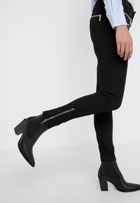 Pantalones negros ajustados con cremalleras laterales combinados con elegantes botines negros de tobillo con tacón cuadrado y punta afilada.