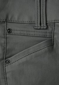 Grått tyg med en slät struktur, som har en ficka med en svart knapp och detaljerad sömnad. Designen inkluderar ett lock för extra förvaring.