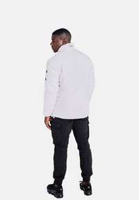 Giacca trapuntata bianca con colletto alto, caratterizzata da un logo sul retro, abbinata a pantaloni cargo neri e sneakers nere.