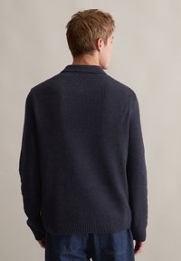 Granatowy sweter dzianinowy o teksturowanej powierzchni, z żeberkowym wykończeniem u dołu i kołnierza. Luźny krój z obniżonymi ramionami i średniej długości rękawami.