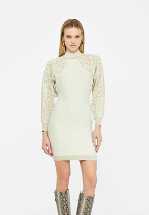 Gebreide jurk in lichtbeige met luipaardpatroon accenten op mouwen en schouders; heeft een hoge kraag en een geribbelde rand.