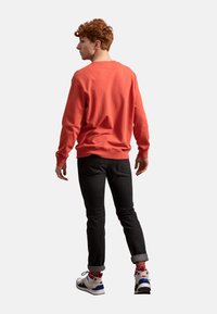 Felpa in cotone corallo con polsini e orlo a costine, abbinata a jeans neri. Le sneaker presentano accenti colorati. Modello visto di spalle.