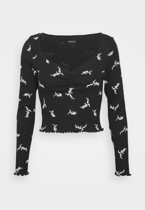 Crop top noir à manches longues avec une finition texturée, présentant un col rond et des motifs floraux blancs ; ourlet et poignets à volants.