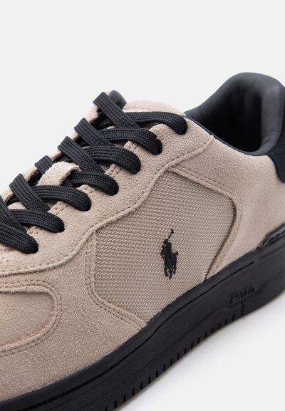 Μπεζ αθλητικό παπούτσι από σουέντ και ύφασμα με μαύρα κορδόνια, μαύρη σόλα και κεντητό λογότυπο αθλητή πόλο στο πλάι.