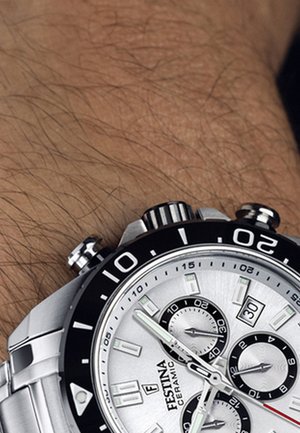 Montre chronographe argentée avec une lunette noire, un bracelet en acier inoxydable et un cadran texturé présentant plusieurs sous-cadrans et des index horaires lumineux.
